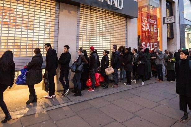 A queue of shoppers waiting outside a large shop for it to open.